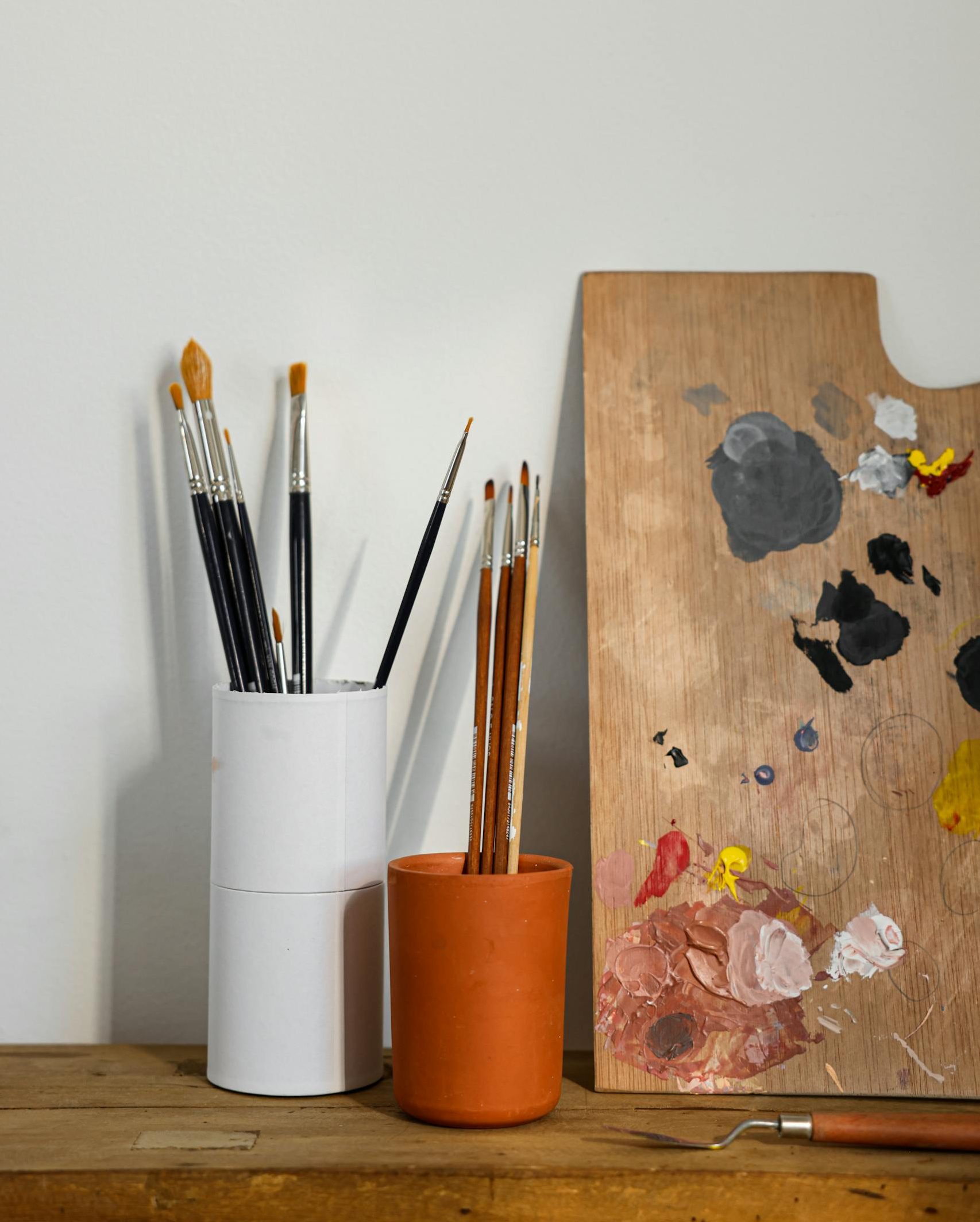 Art supplies arrangement with paint brushes in cups and a colorful palette.