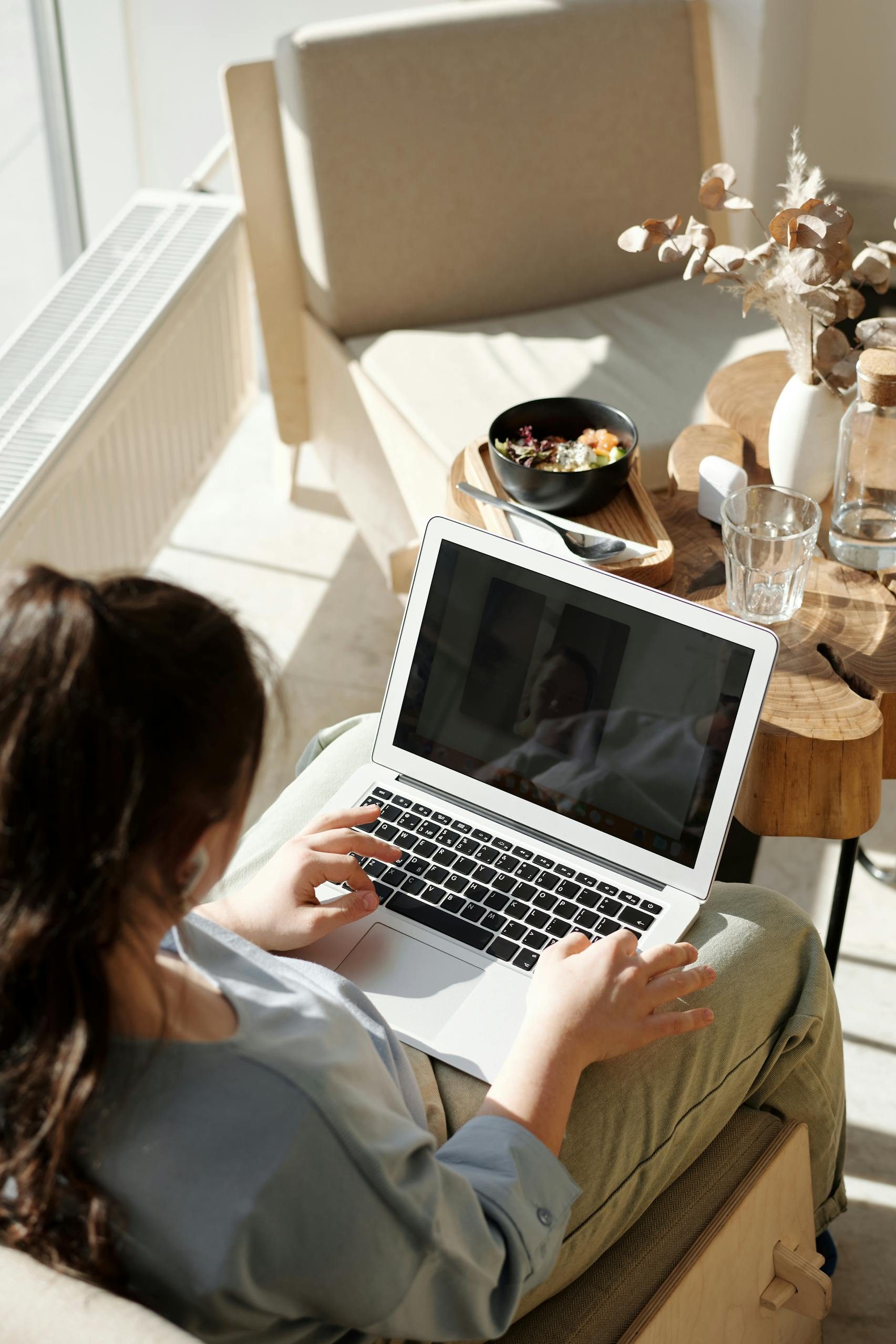 Woman enjoying remote work on a laptop in a cozy home setting with natural light.